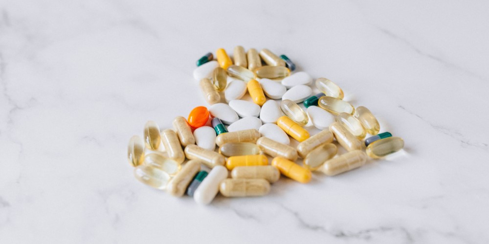 Assorted supplement pills and capsules arranged in a heart shape.