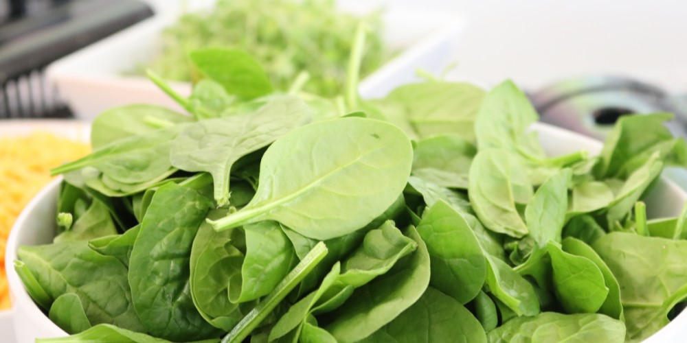 Fresh spinach leaves in a white bowl.
