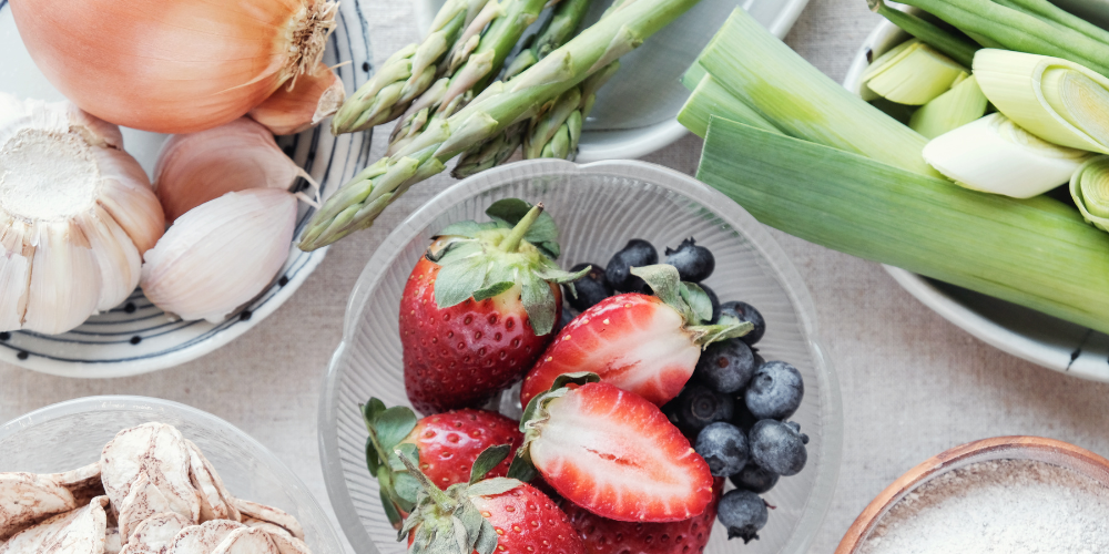 Fresh fruits and vegetables including strawberries, blueberries, asparagus, garlic, and leeks.