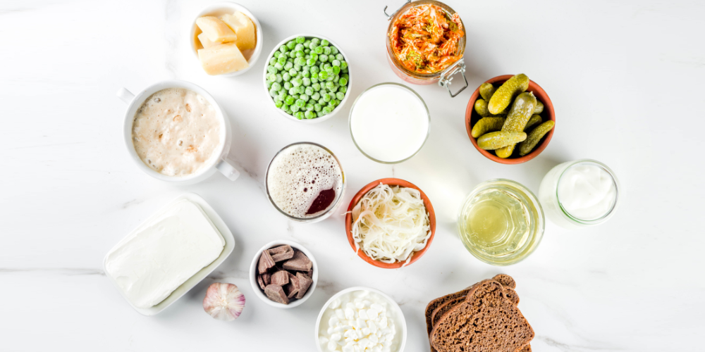 Variety of probiotic foods like yogurt, sauerkraut, kimchi, and pickles on a white table.