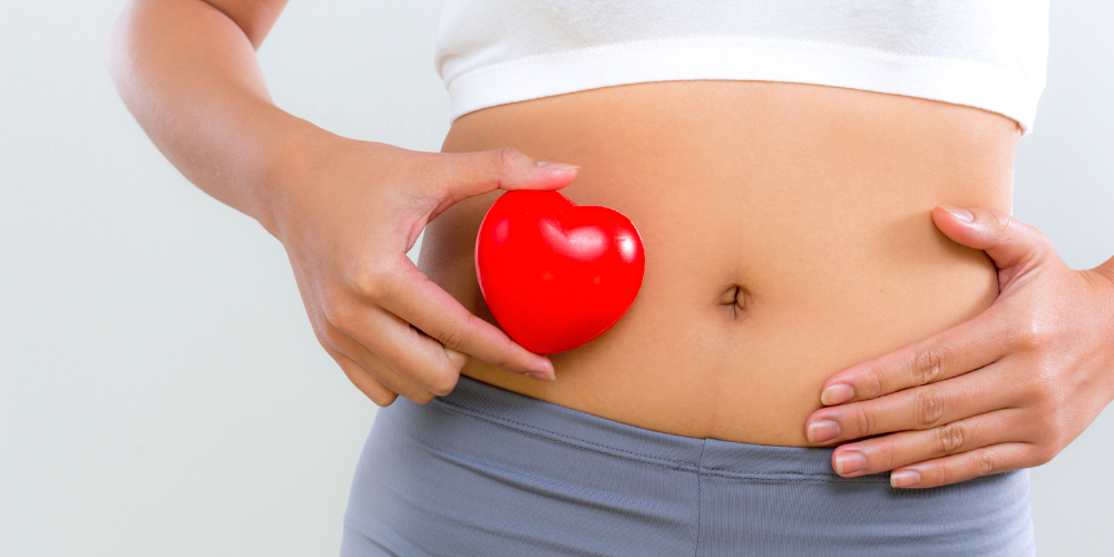 Woman holding a red heart against her stomach.