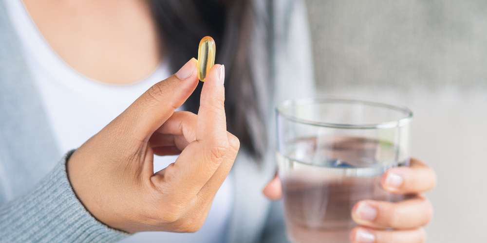 Woman holding a softgel capsule and a glass of water.