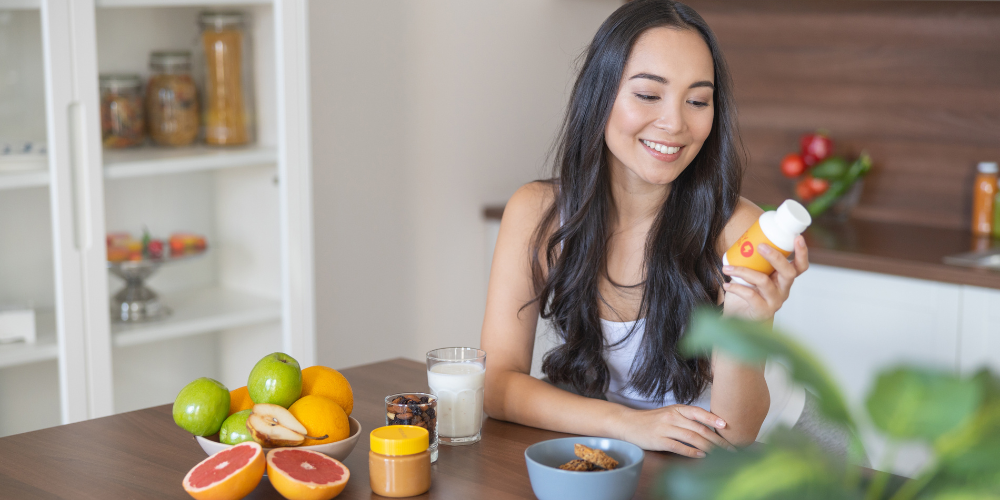 Woman smiling at a supplement bottle with fruit on the table
