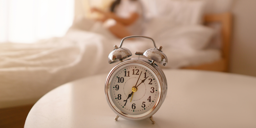 Alarm clock sitting on a white nightstand with person in a bed in the background