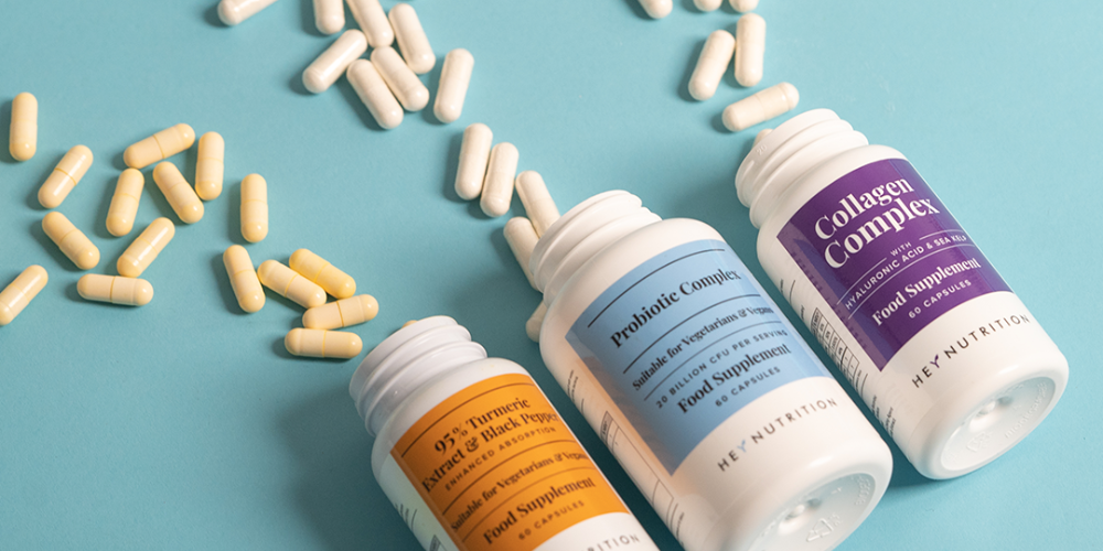 Three Hey Nutrition supplement bottles with capsules scattered on a blue background.